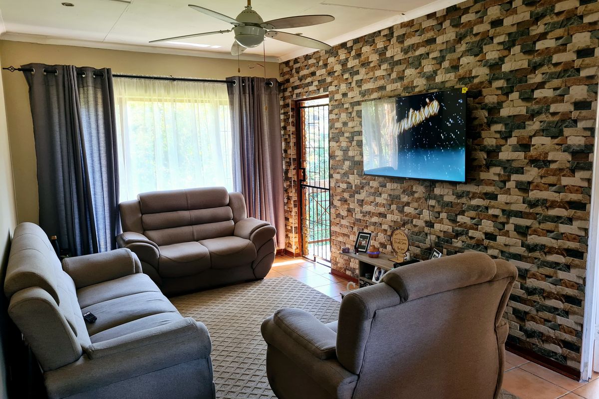 A comfortable living room featuring a textured stone-cladding feature wall, tiled flooring, and a ceiling fan, with direct access to an outdoor area.