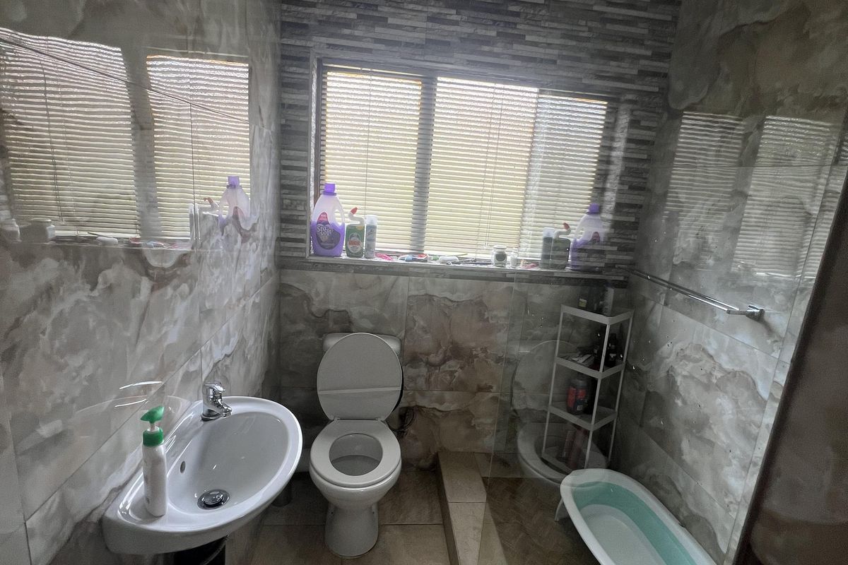 A compact bathroom featuring wall-mounted basin, toilet, and a glass-enclosed shower area with tiled finishes throughout.