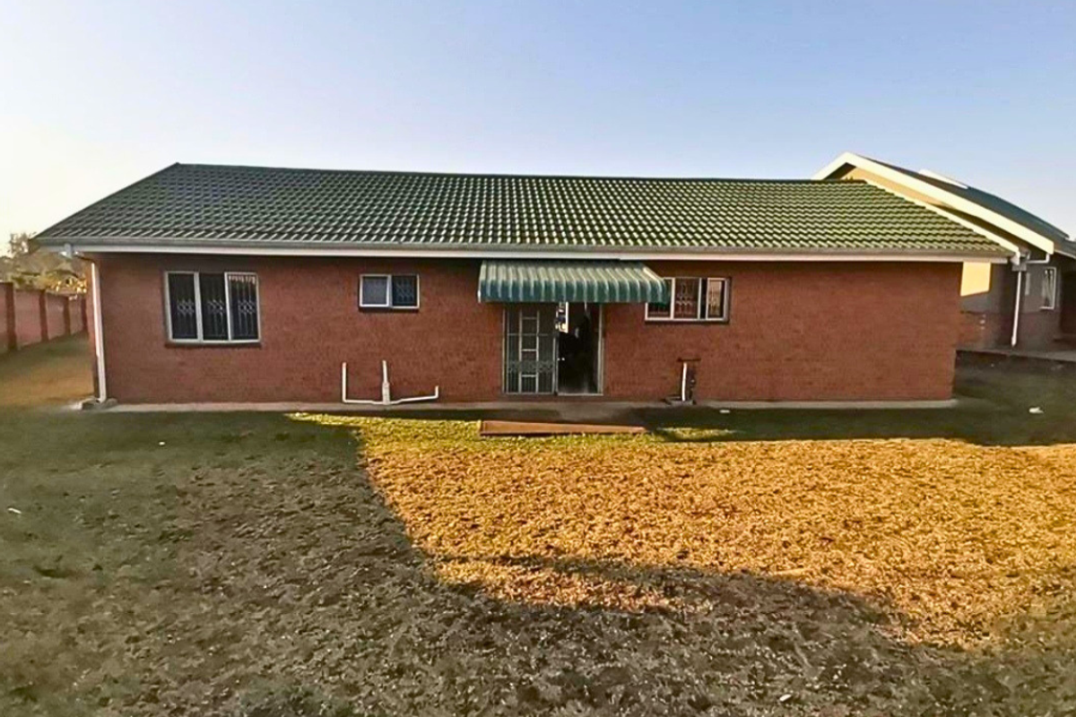 Rear view of a single-story brick apartment building featuring a green tiled roof, metal security window bars, and a small entrance awning.