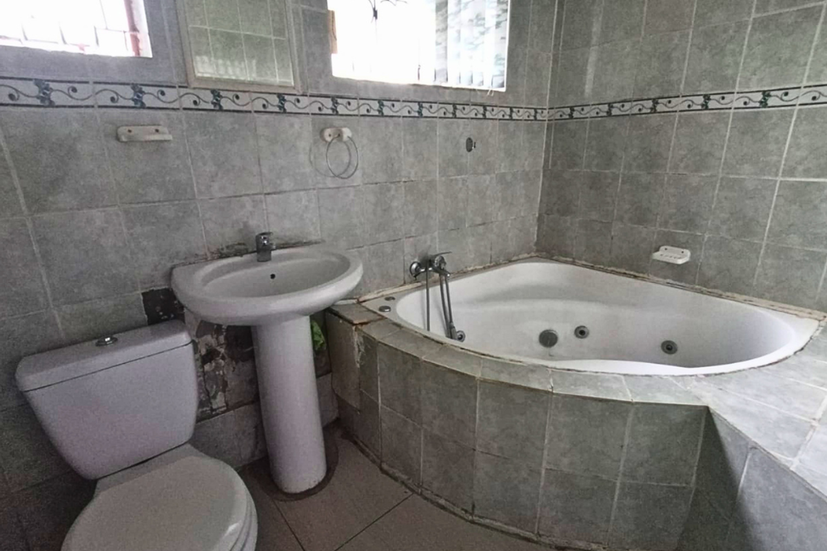 A dated bathroom featuring a corner jetted bathtub, pedestal basin, and toilet with full-height wall tiling.