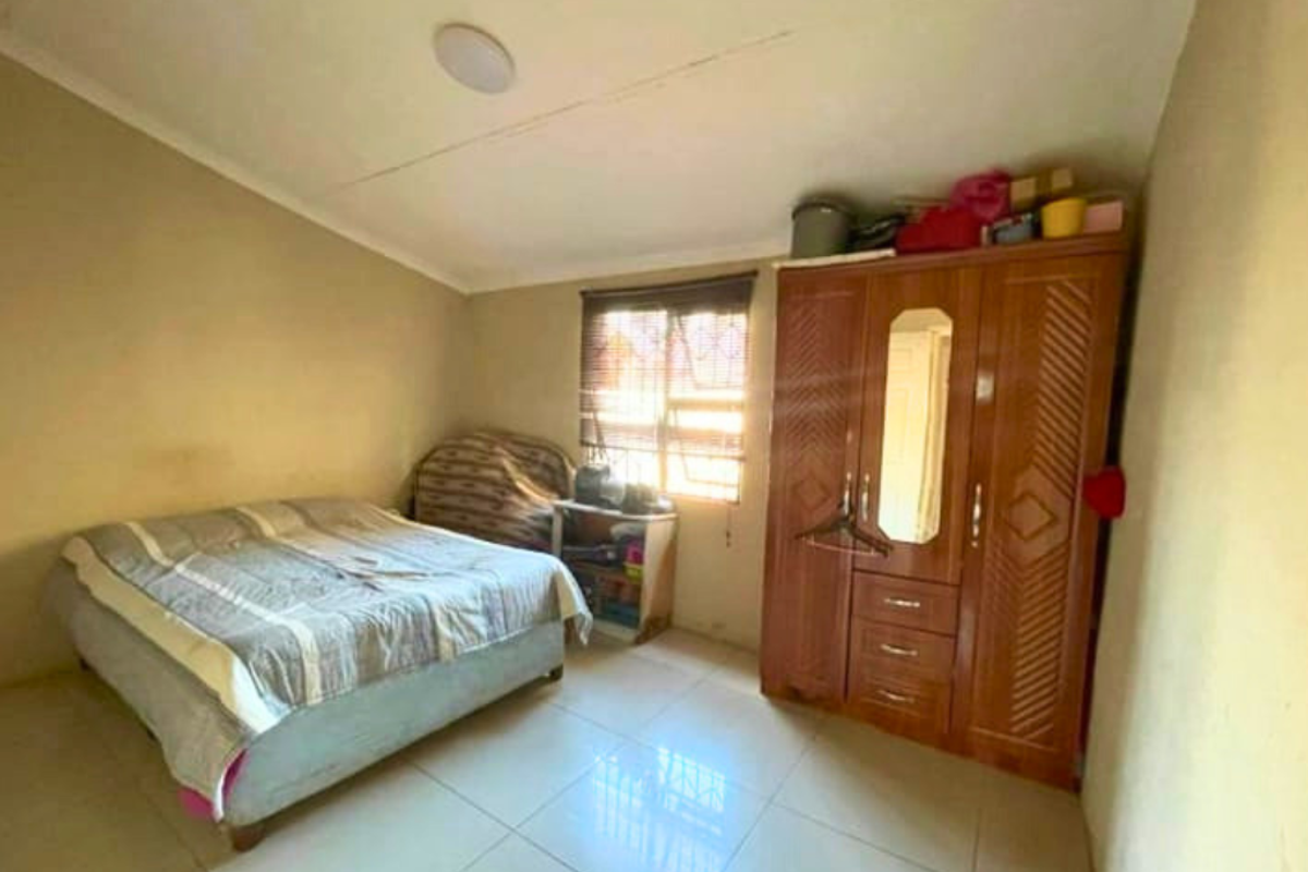 A bedroom featuring tiled flooring, a window with security bars, and a built-in wooden wardrobe.