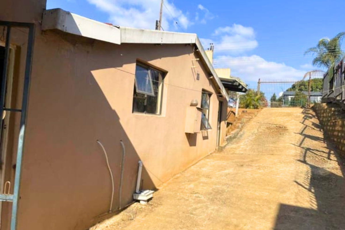 Side exterior view of the property showing a concrete driveway, exterior wall with windows, and basic drainage infrastructure.