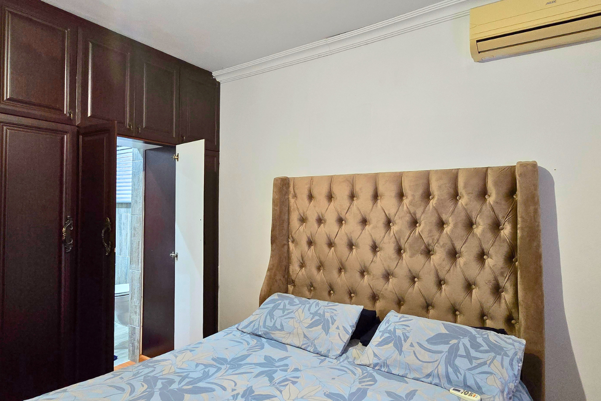 A bedroom featuring dark wood built-in cabinetry and an integrated air conditioning unit, with an adjoining bathroom visible through the open door.