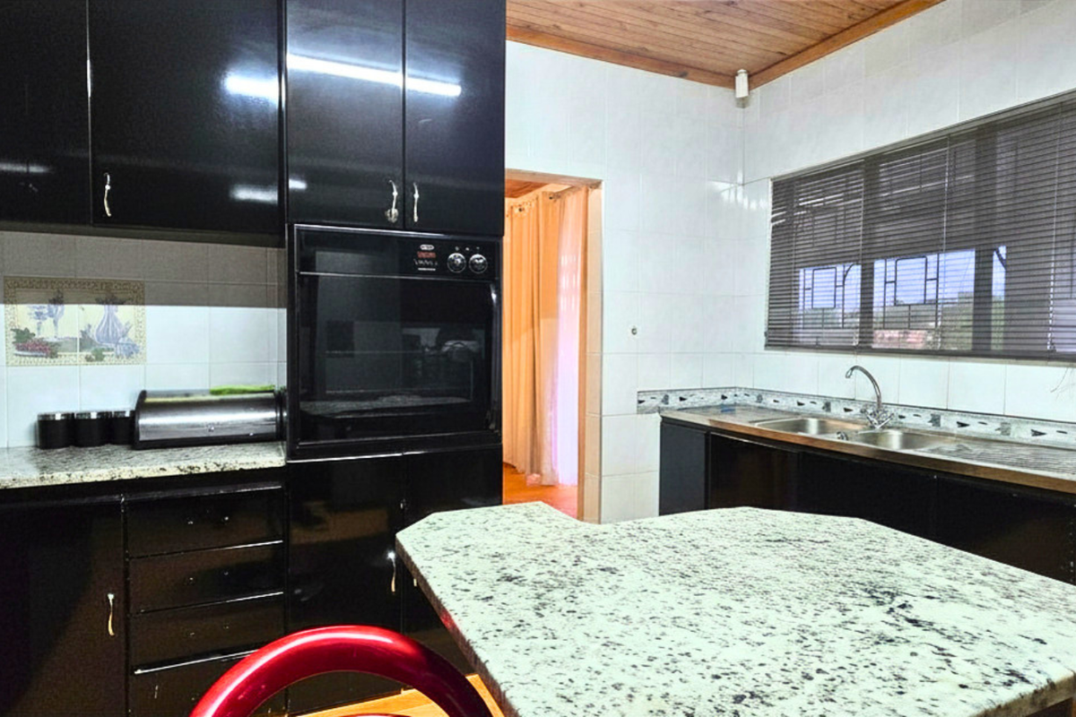 A functional kitchen featuring black cabinetry, granite countertops, a built-in oven, and a double stainless steel sink with tiled splashbacks.