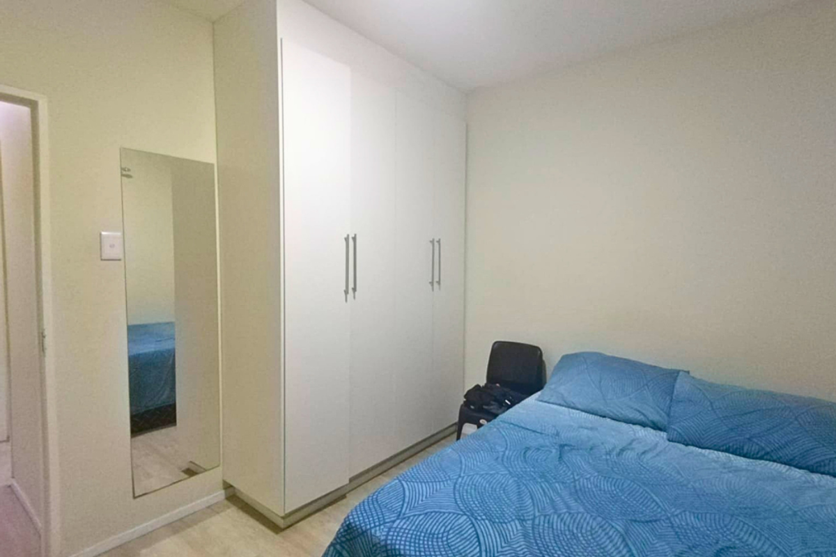 A well-maintained bedroom featuring built-in floor-to-ceiling wardrobes and a wall-mounted mirror, providing ample storage and a clean, functional layout.