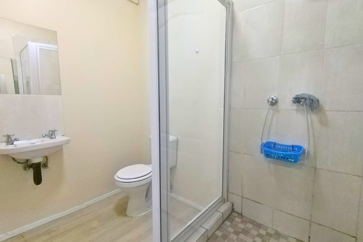 A functional bathroom featuring a glass-enclosed shower, a wall-mounted basin, and a standard toilet with neutral wall tiling.