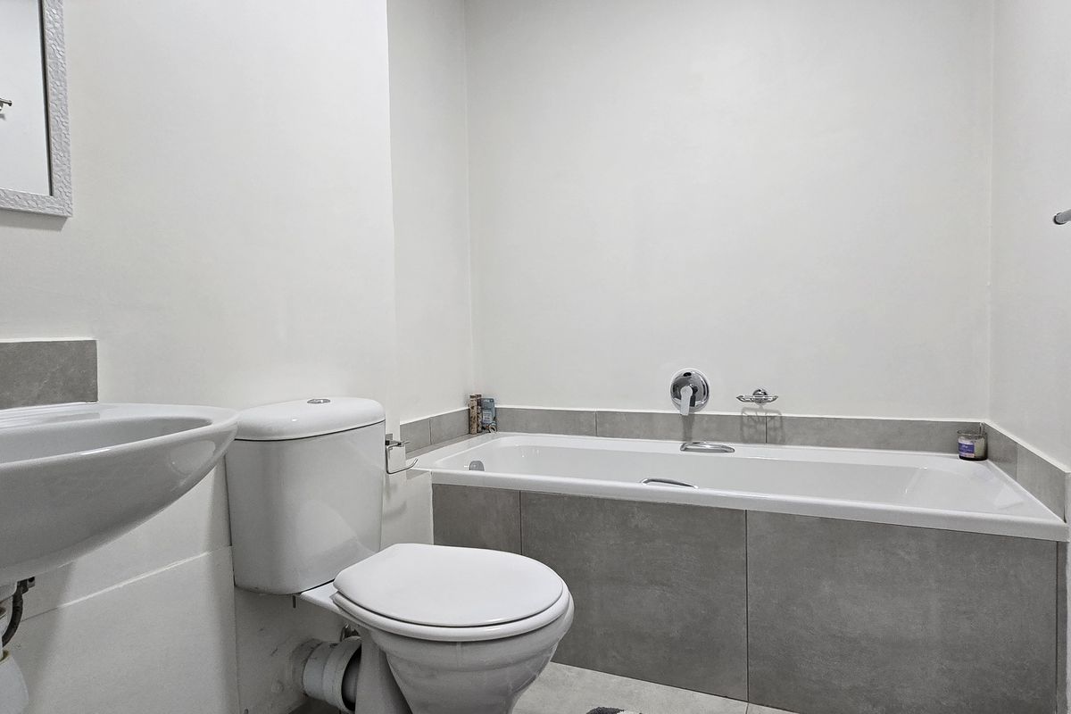 A clean and functional bathroom featuring a built-in bathtub with grey tiling, a pedestal basin, and a standard toilet.