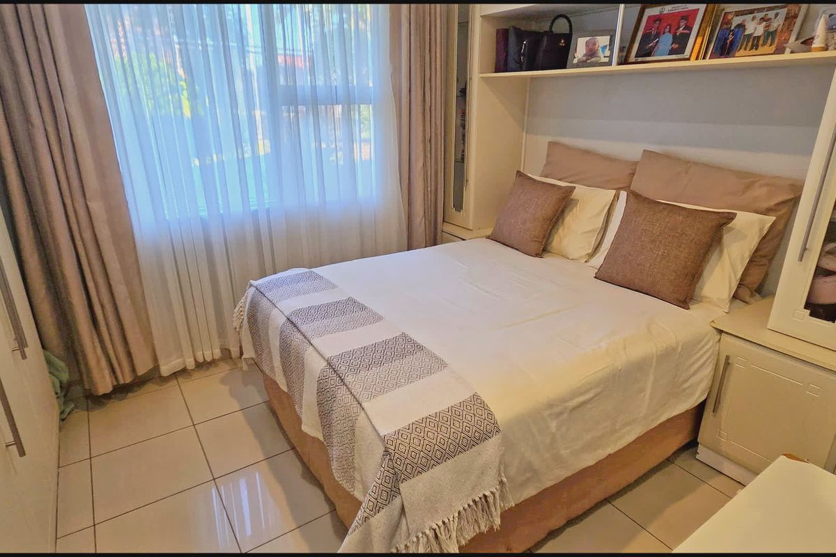 A compact bedroom featuring tiled flooring, built-in cupboards, and integrated headboard shelving with neutral finishes.