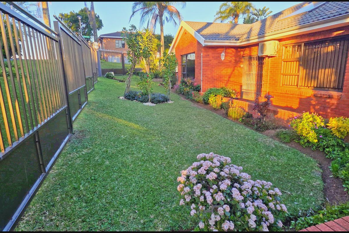 A well-maintained rear garden area featuring a brick facade, secure perimeter fencing, and established landscaping alongside the property exterior.