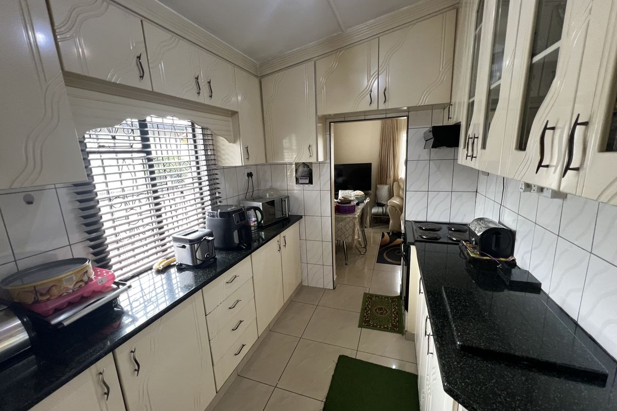 A functional galley-style kitchen featuring dark granite countertops, cream-colored cabinetry, and tiled flooring, with a direct view into the adjacent living area.