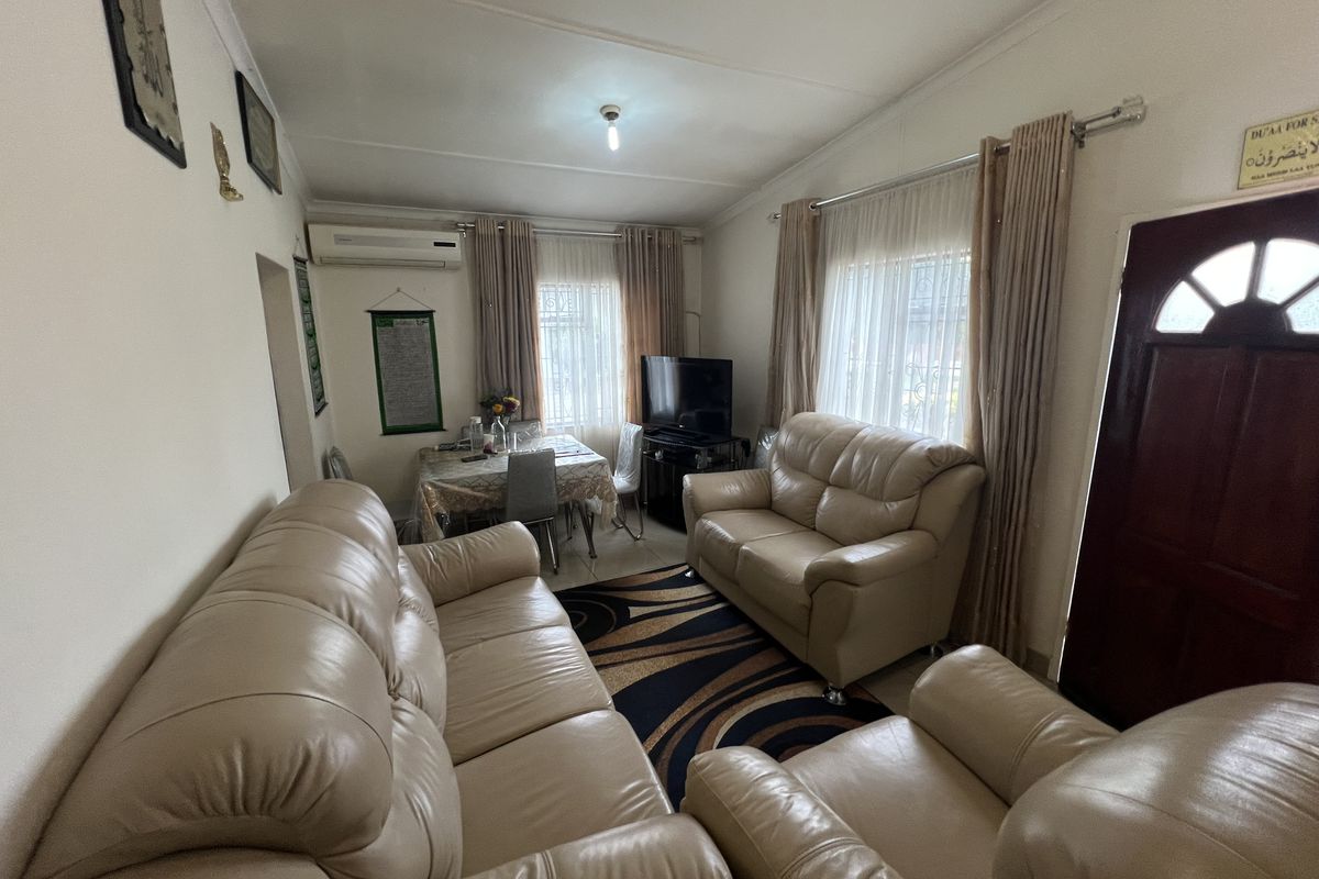 A comfortable living room featuring a wall-mounted air conditioning unit, tiled flooring, and large windows with curtain tracks.