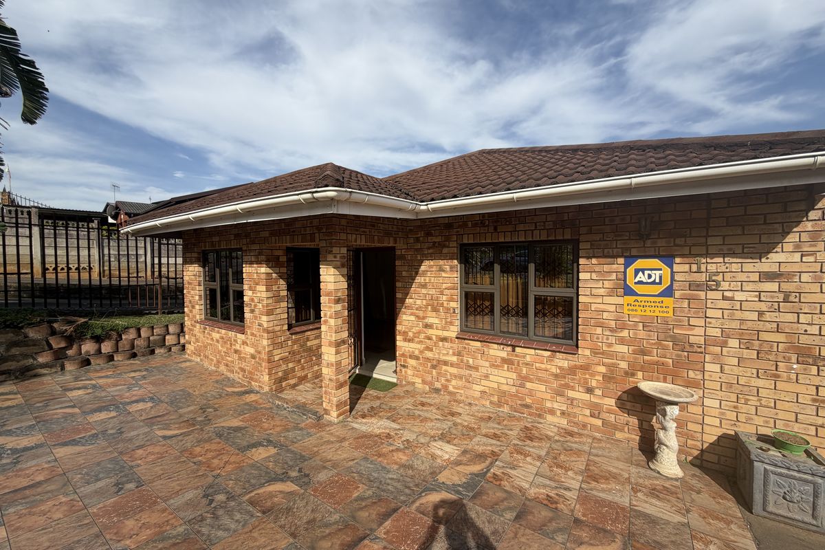A well-maintained face brick exterior featuring a tiled roof, security bars on windows, and a spacious paved patio area.