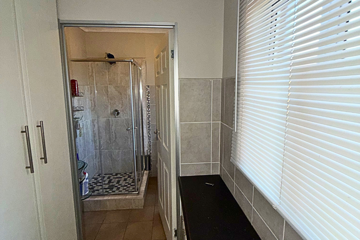 A functional bathroom featuring a glass-enclosed shower with tiled flooring and a vanity area with a dark countertop and window blinds.