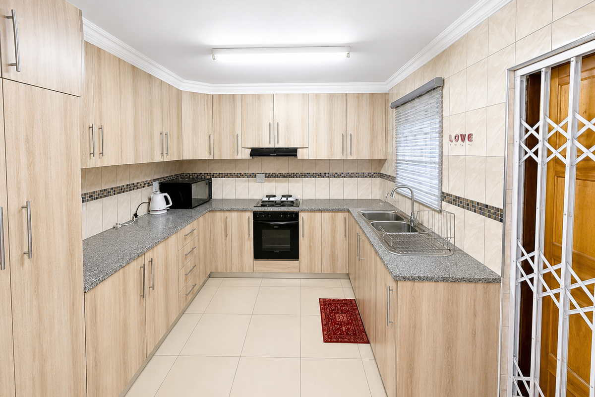 A functional U-shaped kitchen featuring light wood-grain cabinetry, granite countertops, a built-in oven, hob, extractor fan, and a double-basin stainless steel sink.
