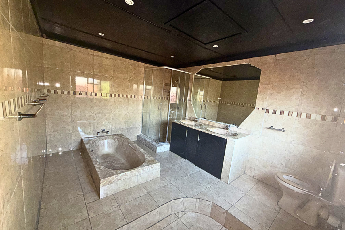 Spacious bathroom featuring a built-in tiled bathtub, glass-enclosed shower, dual vanity with dark cabinetry, and full-wall tiling.