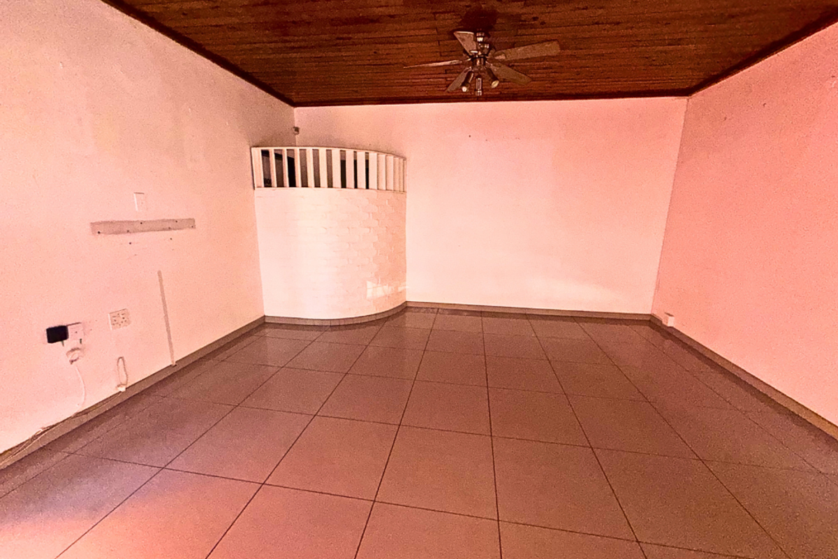 An empty living room featuring tiled flooring, a timber-clad ceiling with a built-in fan, and a unique curved brick feature wall.