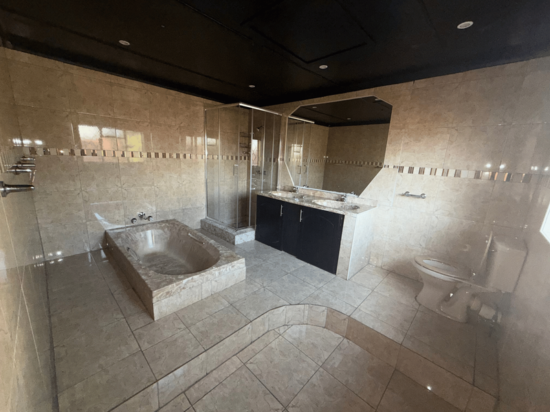 Spacious bathroom featuring a built-in bathtub, glass shower enclosure, double vanity with storage, and neutral floor-to-ceiling tiling.