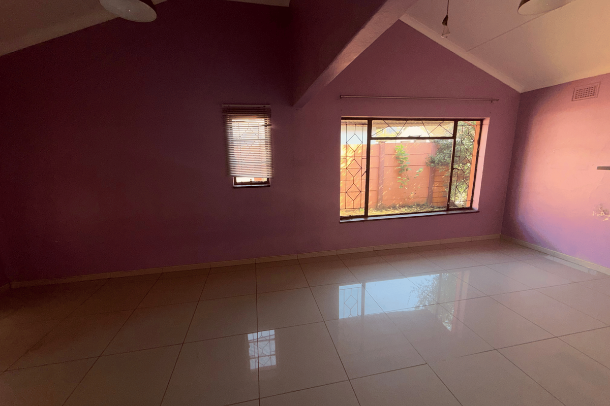 An empty living room featuring vaulted ceilings, large windows with security bars, and polished tiled flooring.