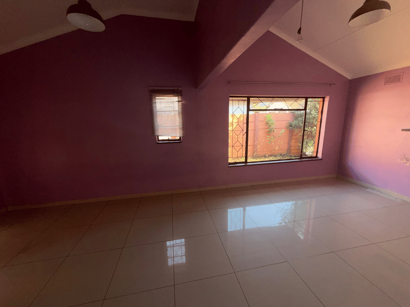 An empty living room featuring vaulted ceilings, large windows with security bars, and polished tiled flooring.