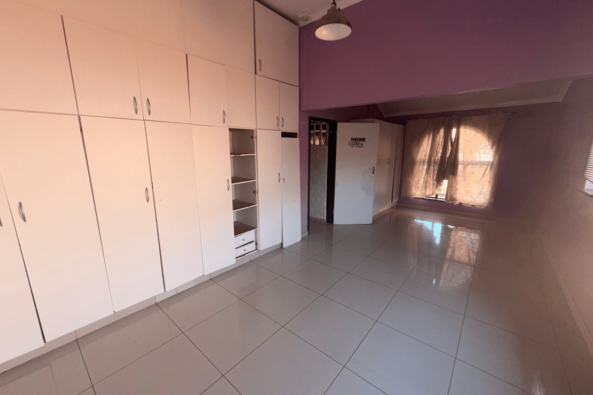 Spacious bedroom featuring extensive built-in cupboards, neutral tiled flooring, and a large window, offering a blank canvas for personalization.