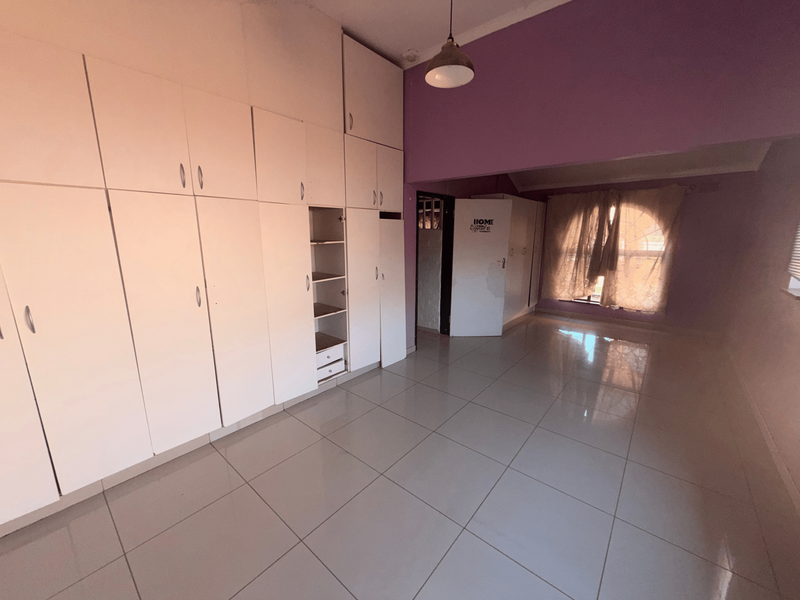 Spacious bedroom featuring extensive built-in cupboards, neutral tiled flooring, and a large window, offering a blank canvas for personalization.