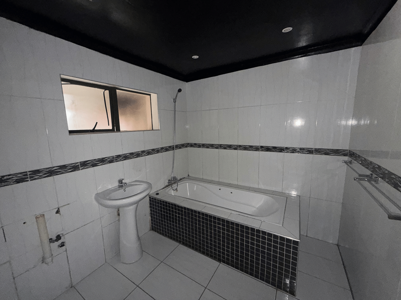 A bathroom featuring a pedestal basin and a built-in bathtub with tiled finishes. The space requires minor repairs to exposed plumbing and wall tiling.