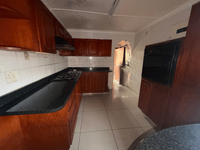 A dated kitchen featuring dark wood cabinetry, black granite countertops, built-in oven, and tiled finishes, offering significant potential for a modern renovation.