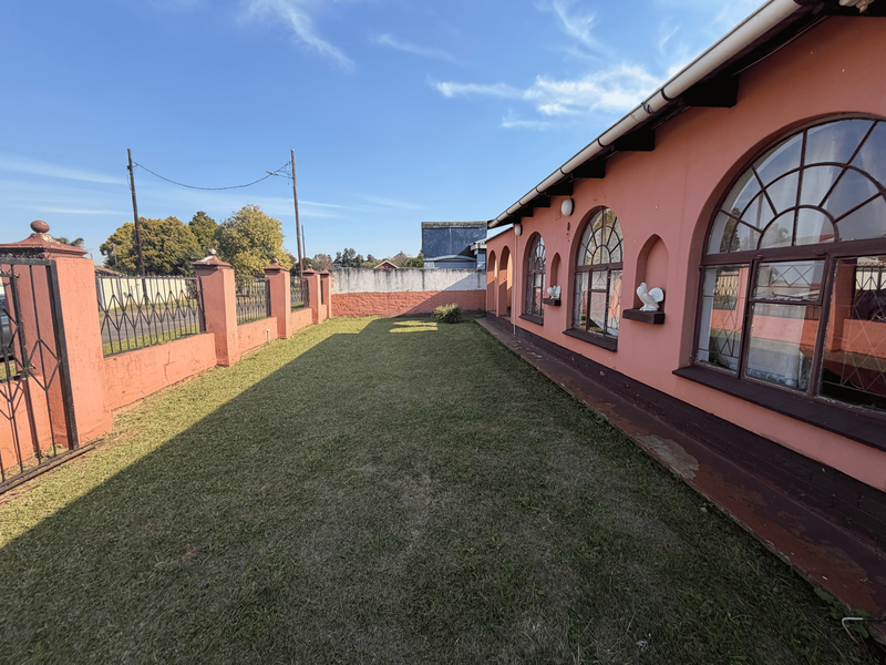 A rear garden area featuring a lawn, perimeter wall with wrought iron gate, and a building facade with distinctive arched windows.