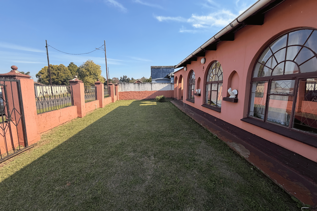 A rear garden area featuring a lawn, perimeter wall with wrought iron gate, and a building facade with distinctive arched windows.