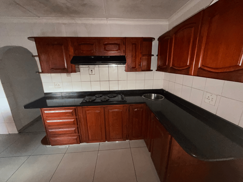 A functional kitchen featuring dark wood cabinetry, black granite countertops, a built-in hob with extractor fan, and tiled finishes throughout.