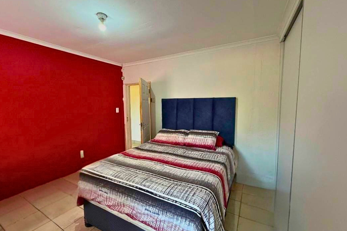 A bedroom featuring tiled flooring, built-in cupboards, and a bold red accent wall.