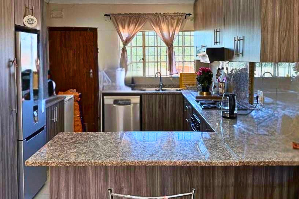 A functional kitchen featuring granite countertops, wood-grain cabinetry, a built-in hob, extractor fan, and an integrated dishwasher space.