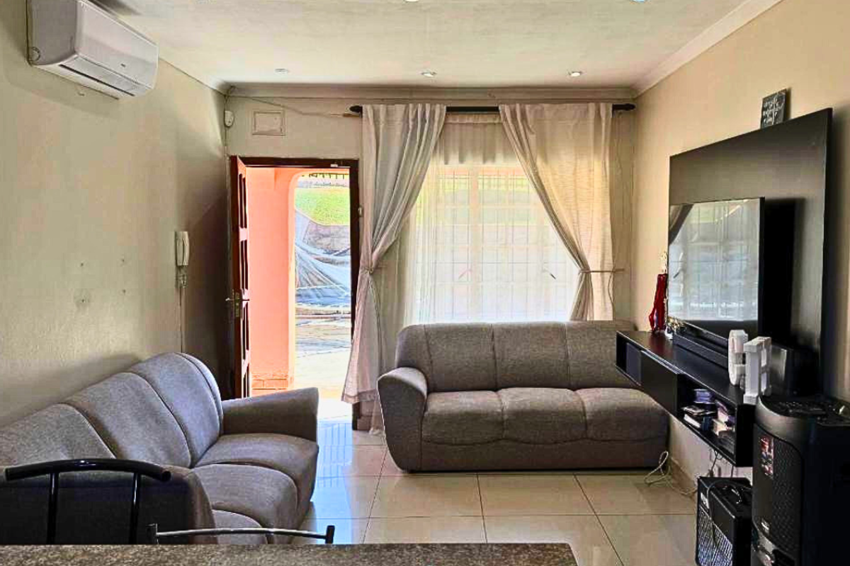 A comfortable living room featuring tiled flooring, recessed ceiling lighting, and a wall-mounted air conditioning unit, with direct access to an outdoor area.