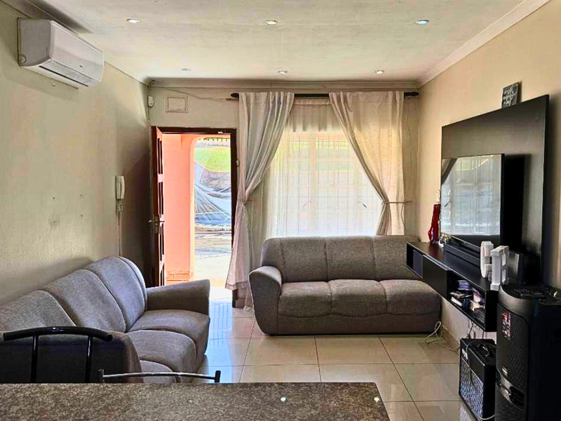A comfortable living room featuring tiled flooring, recessed ceiling lighting, and a wall-mounted air conditioning unit, with direct access to an outdoor area.