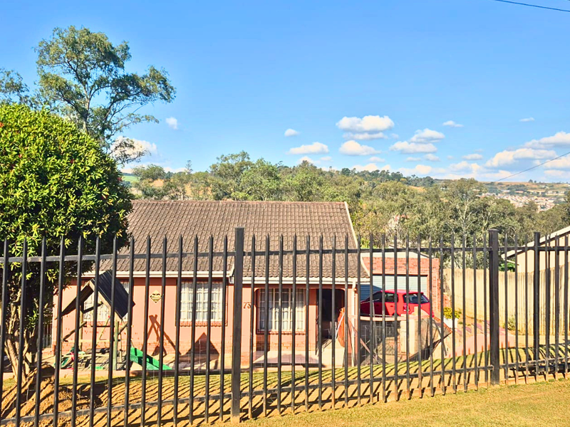 A view of the front elevation of a single-story brick house featuring a tiled roof, security fencing, and a driveway.