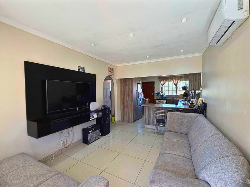 Open-plan living area featuring tiled flooring, a wall-mounted air conditioning unit, and a breakfast bar connecting to the kitchen space.
