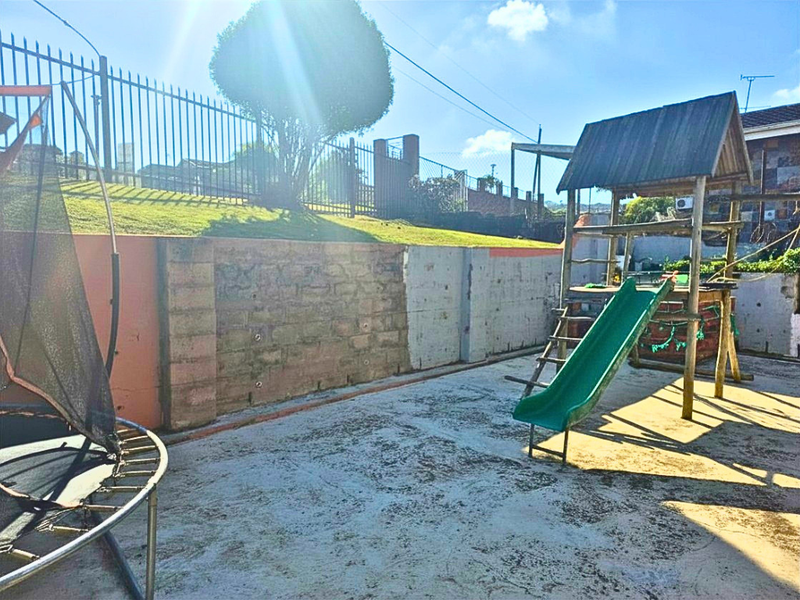Outdoor backyard area featuring a concrete patio, a retaining wall, and a wooden play structure with a slide.