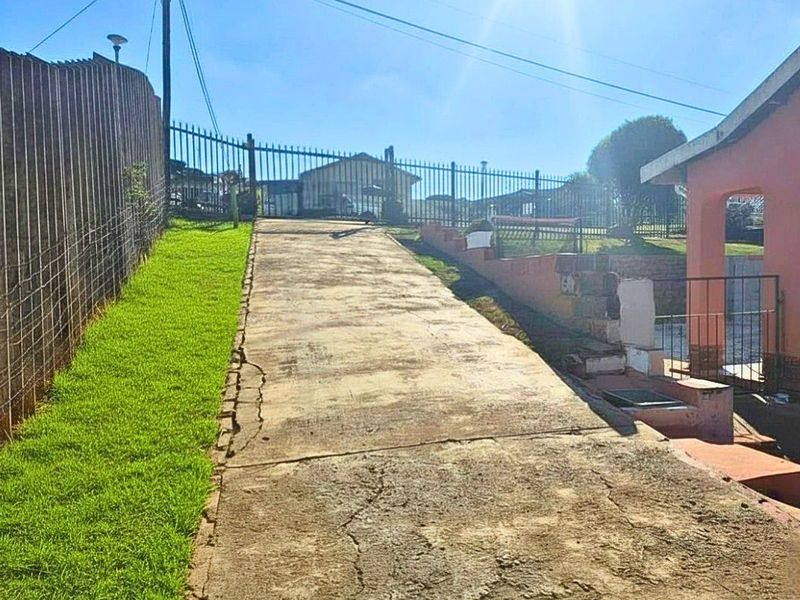 A sloped concrete driveway leading to the property entrance, featuring perimeter metal security fencing and a retaining wall structure.
