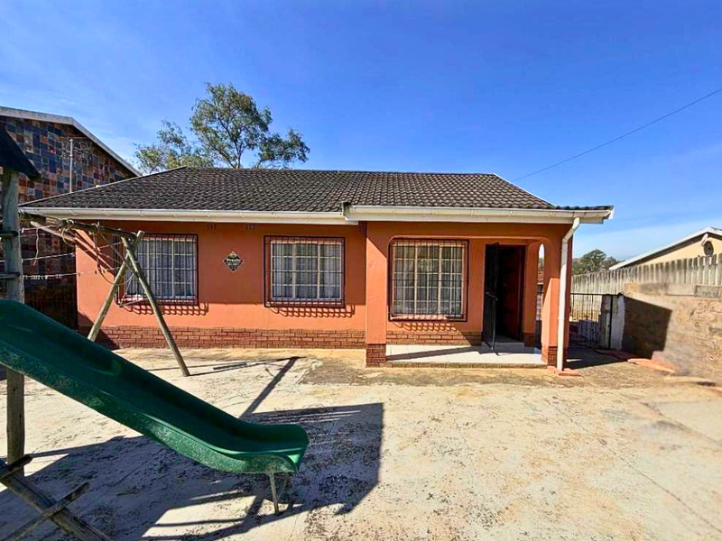 Rear view of a single-story house featuring a tiled roof, brick base detailing, and security bars on windows, set within a paved backyard area.