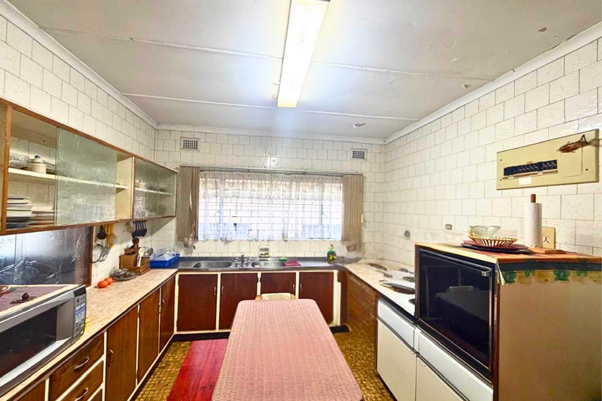 A dated kitchen featuring original cabinetry, tiled walls, and a functional layout with built-in oven and double sink.