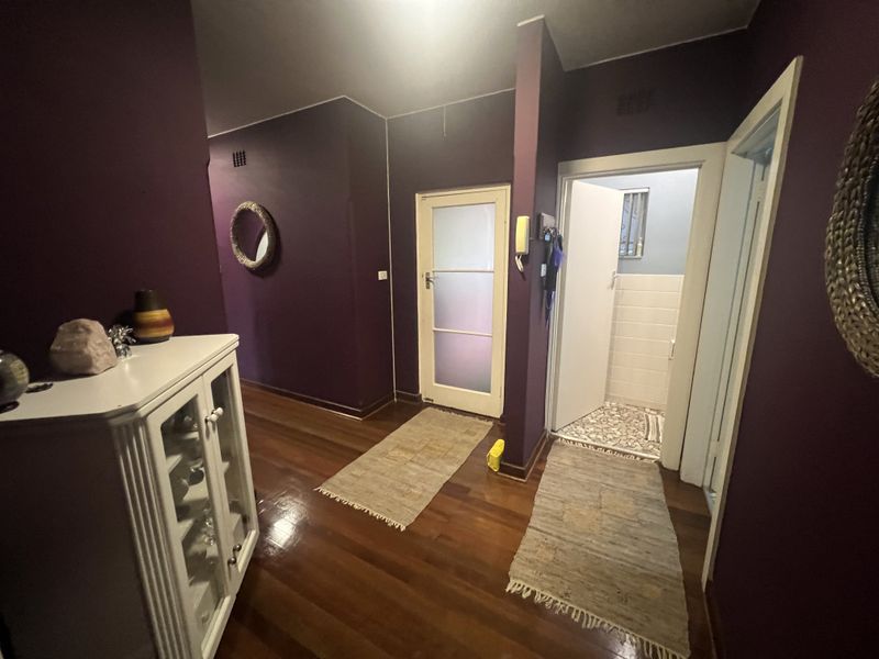 A hallway featuring dark purple walls, polished timber flooring, and access to an adjacent tiled bathroom area.
