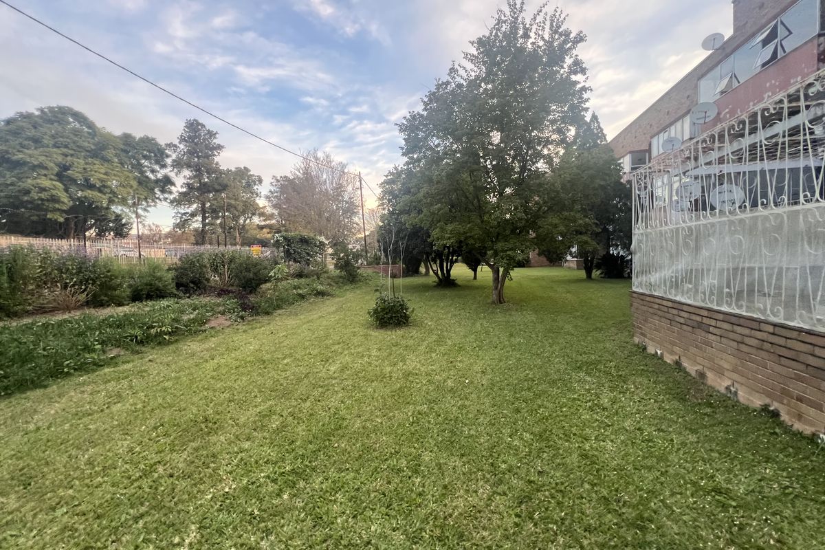 A spacious rear garden area featuring a well-maintained lawn, mature trees, and a brick-built townhouse exterior with security gates.