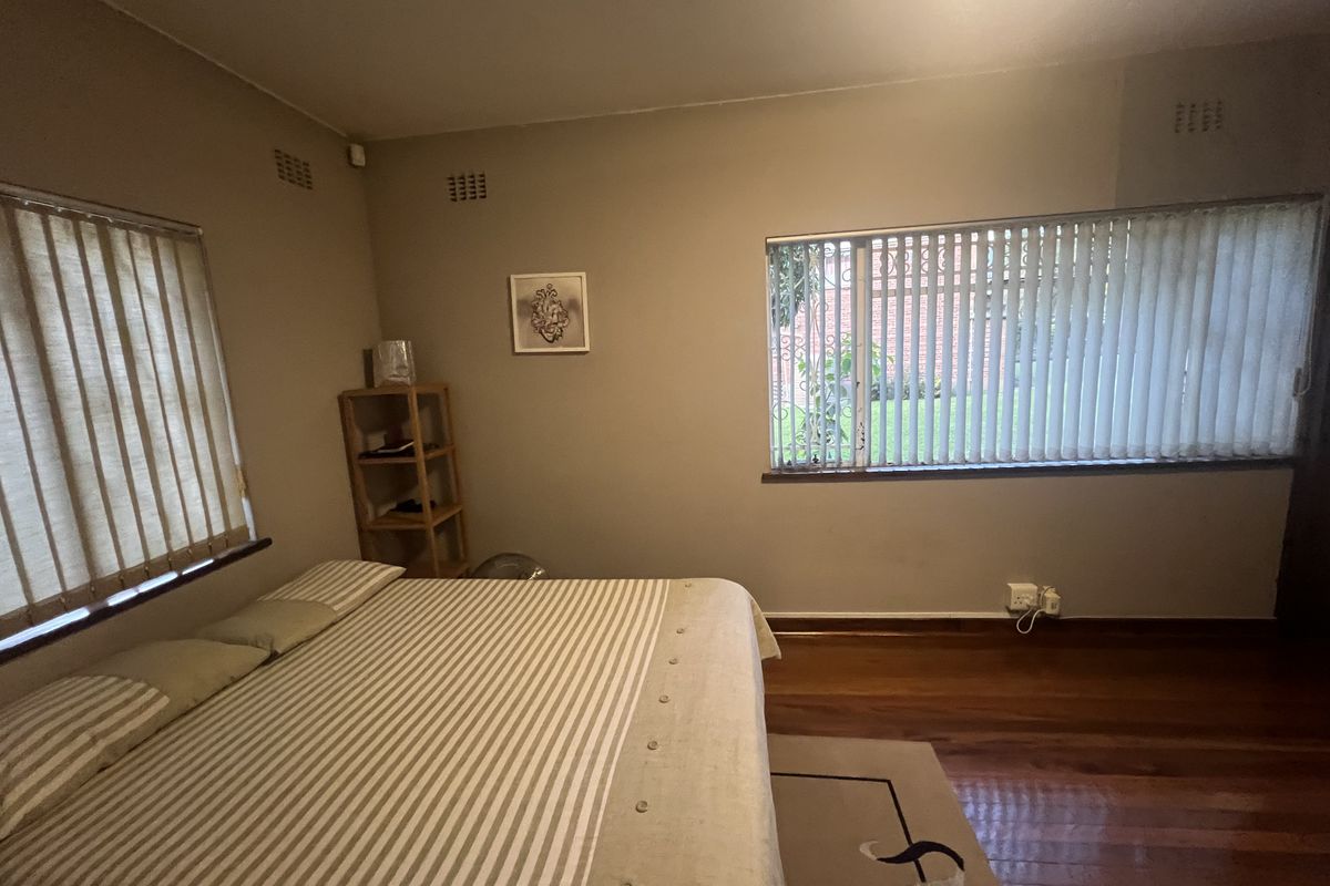 A bedroom featuring hardwood flooring, vertical blinds on windows, and security bars, offering a functional space with neutral wall tones.