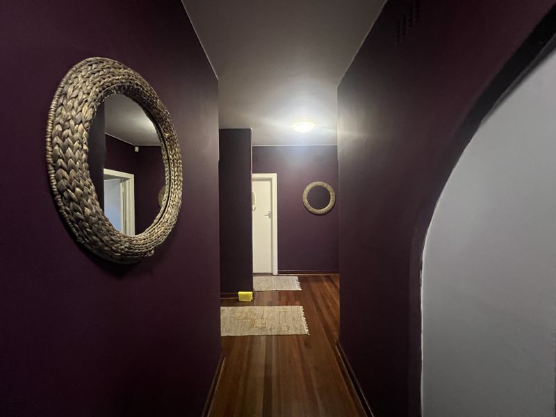 A hallway featuring dark-toned walls and polished timber flooring, leading to an interior doorway.