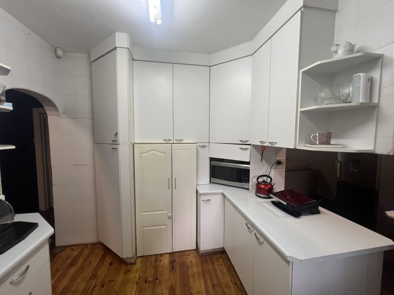 A functional kitchen featuring white cabinetry, built-in microwave, and timber flooring, offering a clean layout with ample storage space.