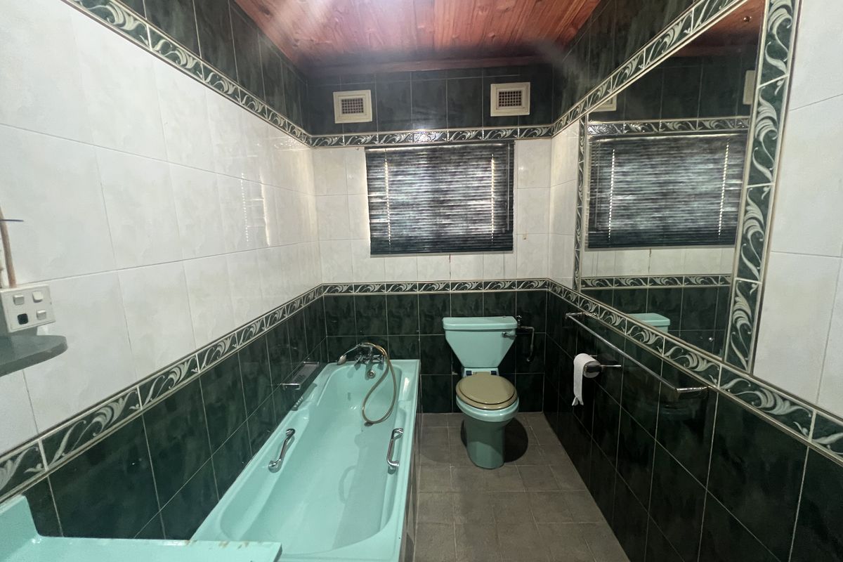 A dated bathroom featuring a mint green bathtub and toilet, dark green wall tiles, and a timber-paneled ceiling.