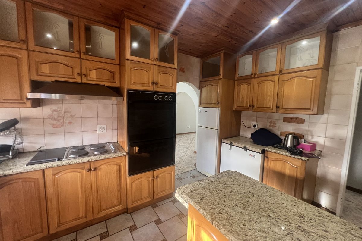 A traditional kitchen featuring wooden cabinetry, granite countertops, a built-in oven, and a tiled backsplash, leading into an adjacent living area.