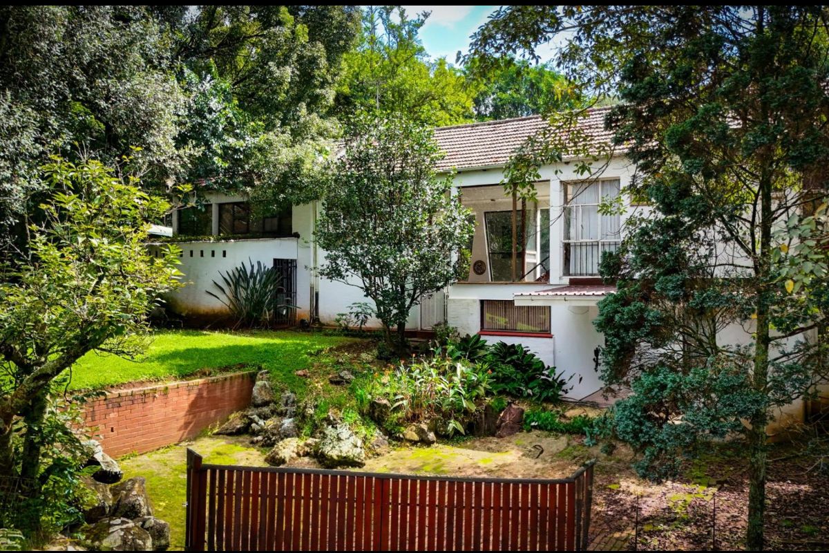 Rear view of the property featuring a multi-level facade, established garden, brick retaining wall, and mature trees providing a private outdoor setting.