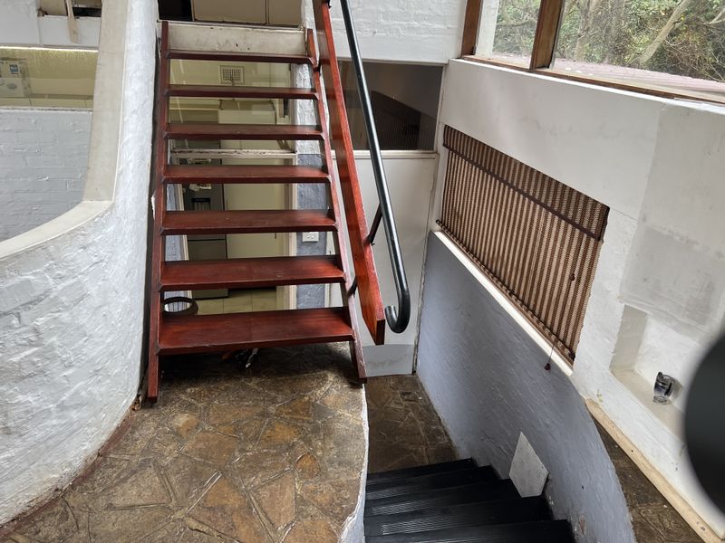 A split-level interior staircase featuring timber treads, a metal handrail, and stone-tiled landing, connecting different levels of the home.