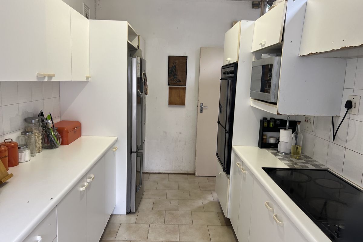 Galley-style kitchen featuring white cabinetry, built-in oven, electric cooktop, and tiled flooring, offering a functional layout with potential for modernization.
